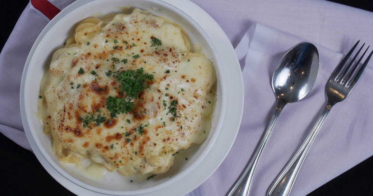 Delicious creamy baked pasta topped with parsley and served on a white napkin.