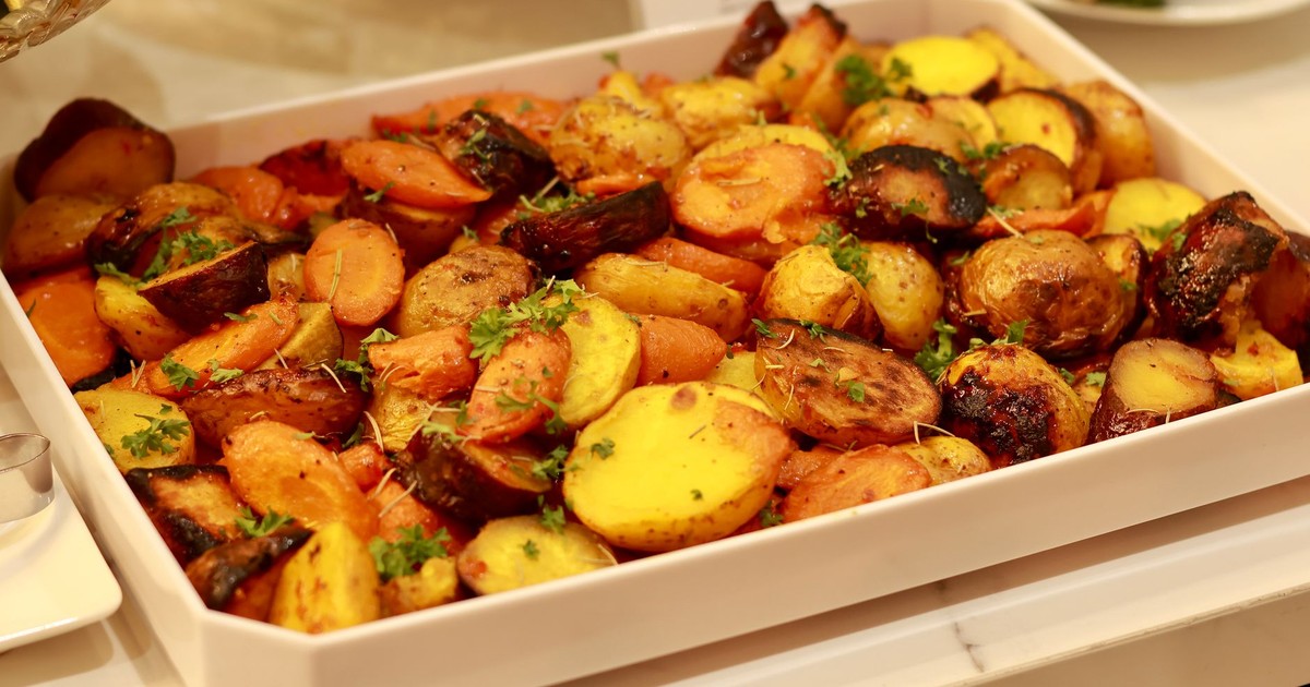 Colorful roasted potatoes and carrots garnished with herbs in a baking tray.