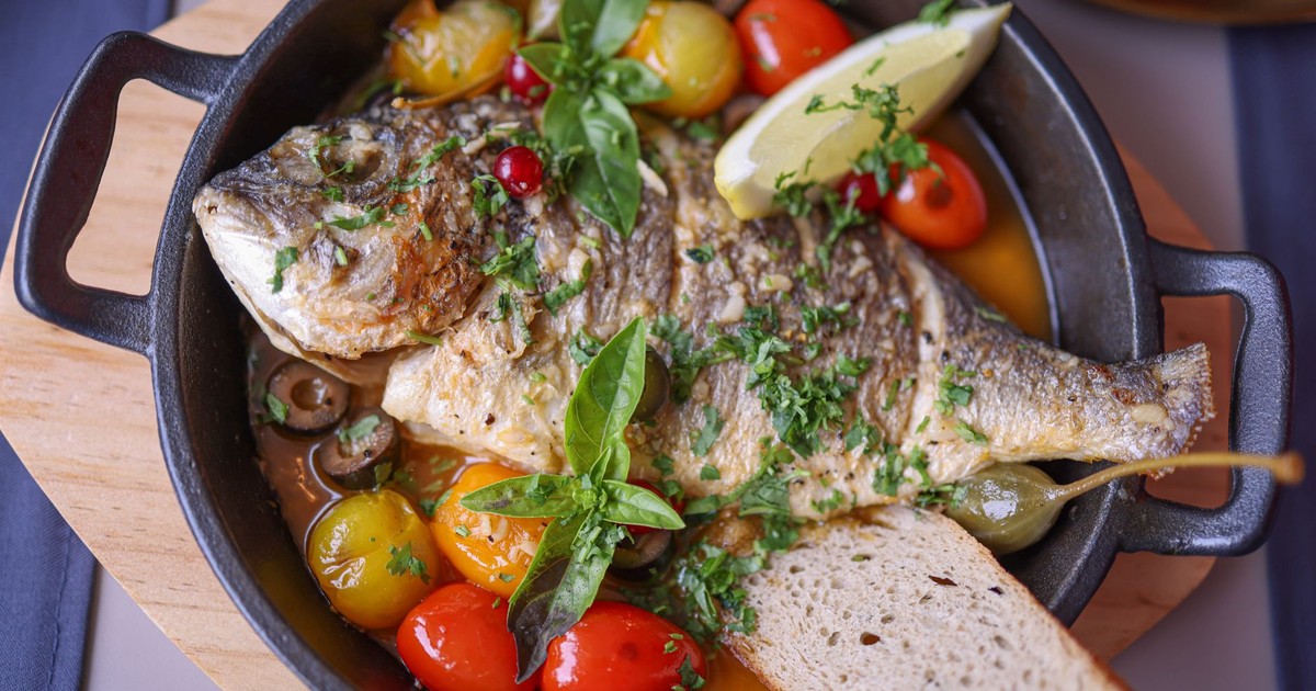 Delicious roasted fish with basil, tomatoes, olives, and lemon slice in rustic presentation.