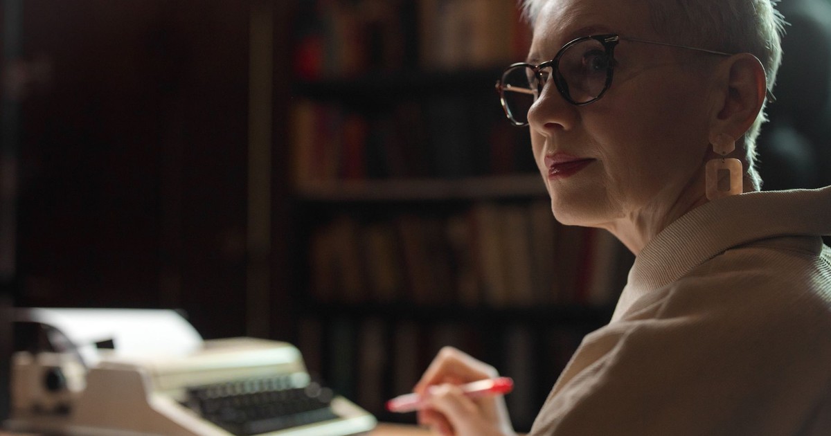 Elderly woman with glasses writing in an office with a vintage typewriter.