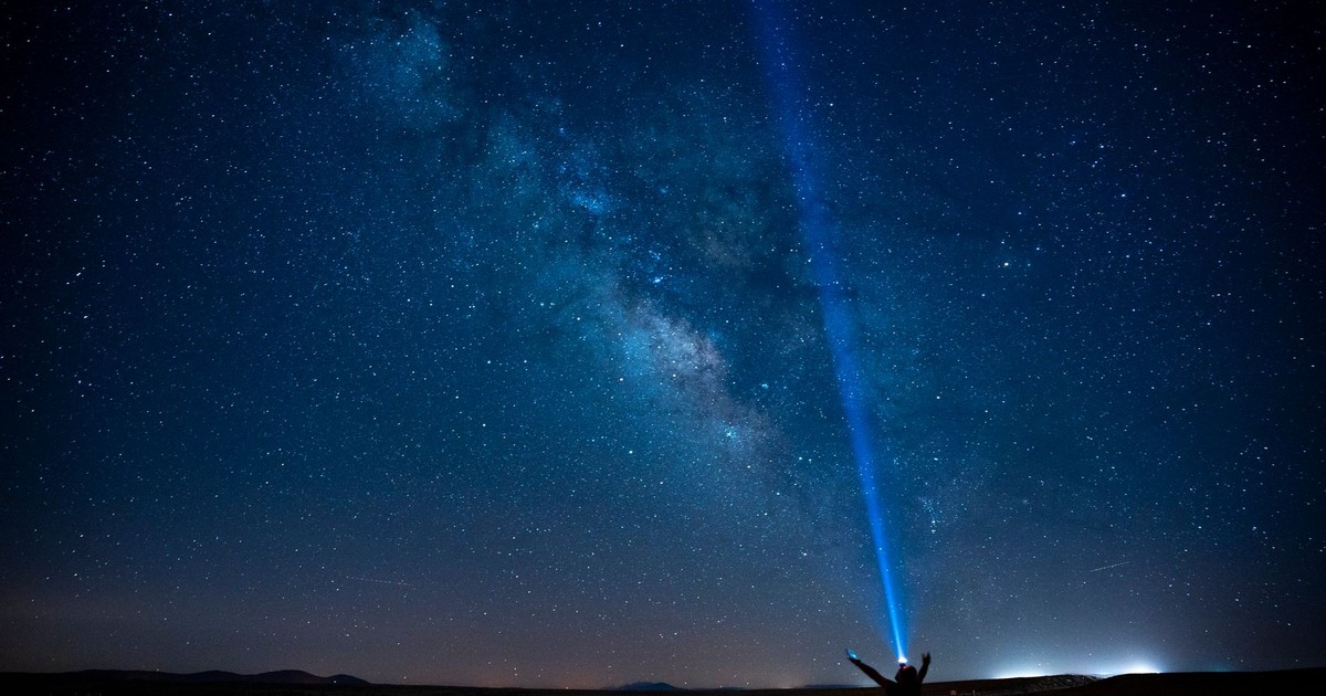 A person stands on a road under the Milky Way, pointing a beam of light into the starry night sky in Karaman, Türkiye.
