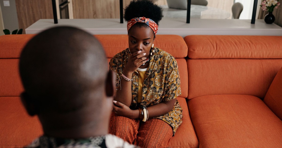 A thoughtful couple seated on a vibrant orange couch in a cozy living room setting.