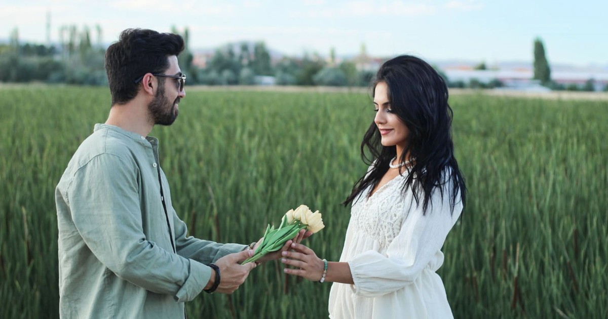 A man and woman share a bouquet, expressing love in a lush green field.