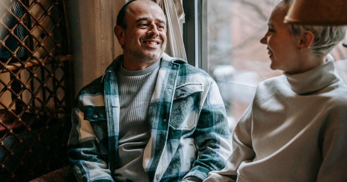 Glad man in checkered casual shirt speaking with positive crop woman near window in daytime