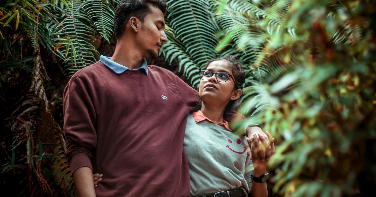 A young couple shares an affectionate moment in a vibrant forest setting.
