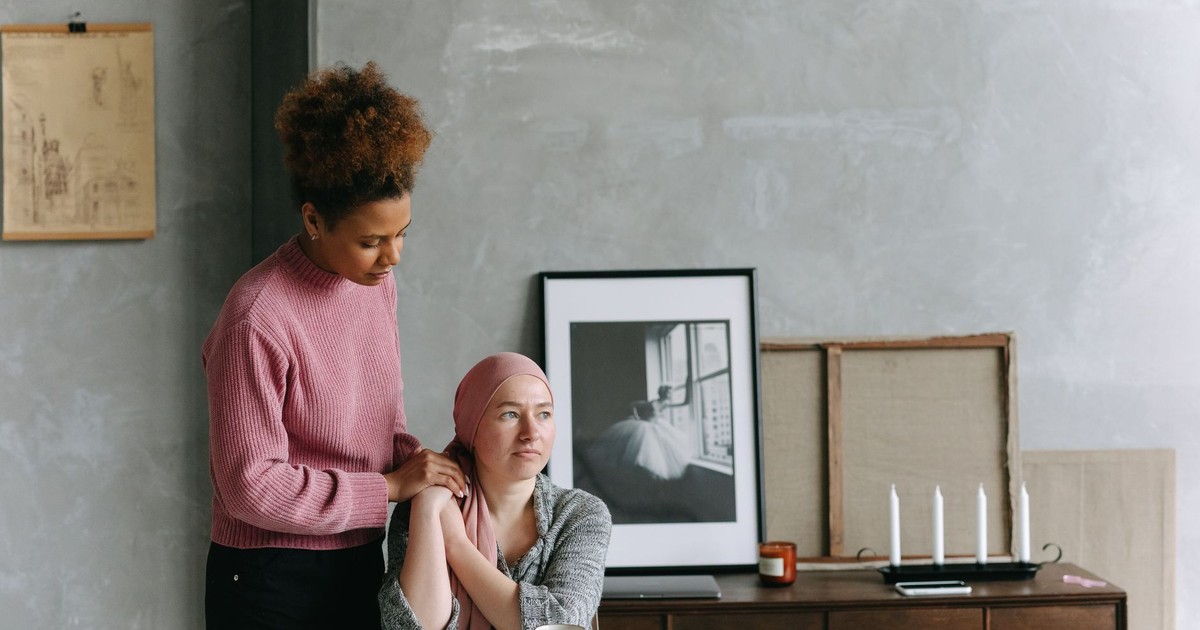 A supportive friend comforts a woman with a headscarf, showing empathy and care.