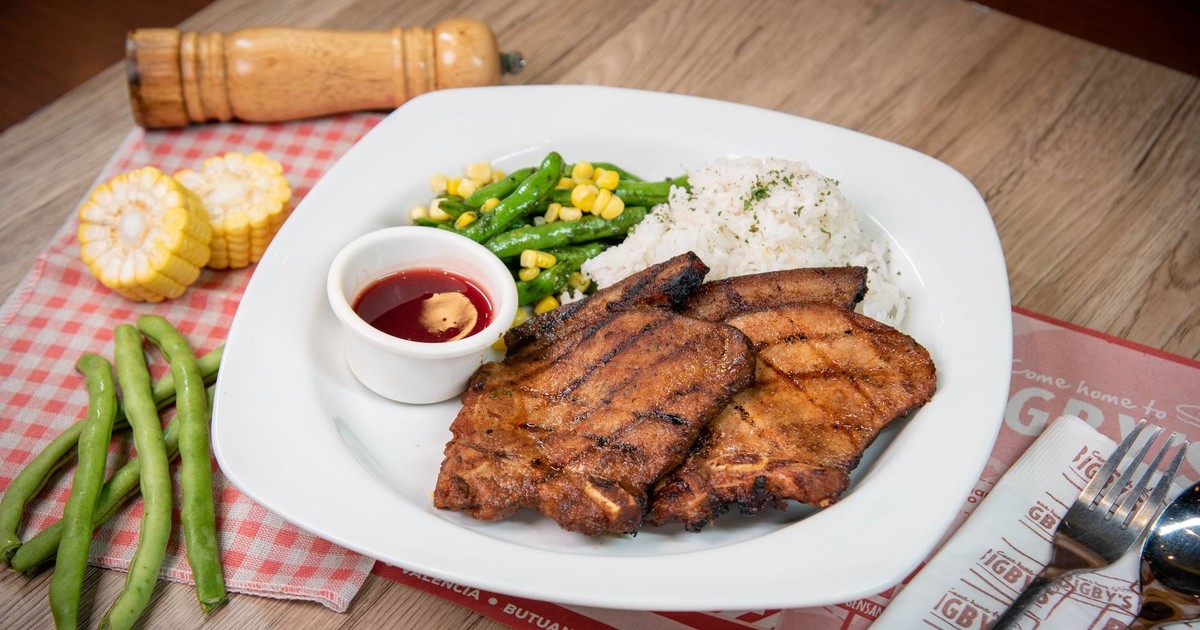 Delicious grilled pork chops served with rice, green beans, and corn on a dining table.