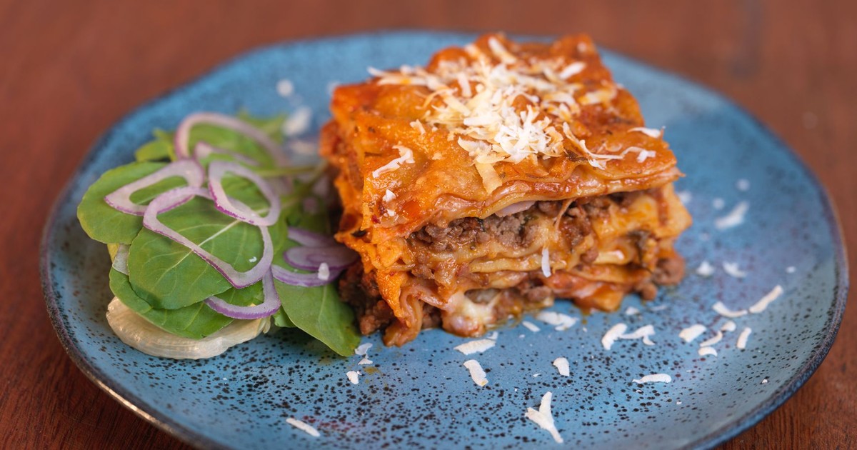 Mouth-watering homemade lasagna with salad served on a rustic blue ceramic plate.