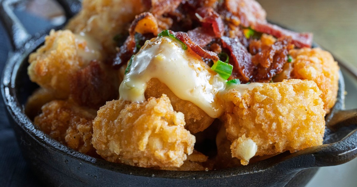 Crispy tater tots topped with melted cheese and bacon in a skillet.