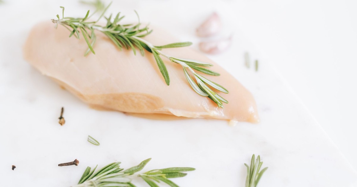 Healthy raw chicken breast garnished with rosemary on a marble surface.