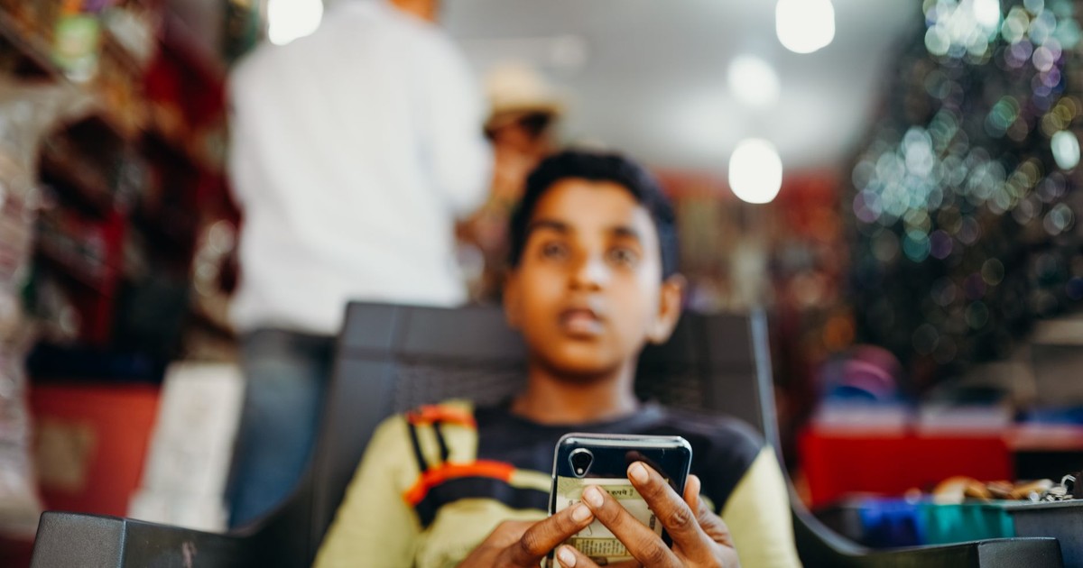 A young boy focused on his smartphone indoors with a blurred background.