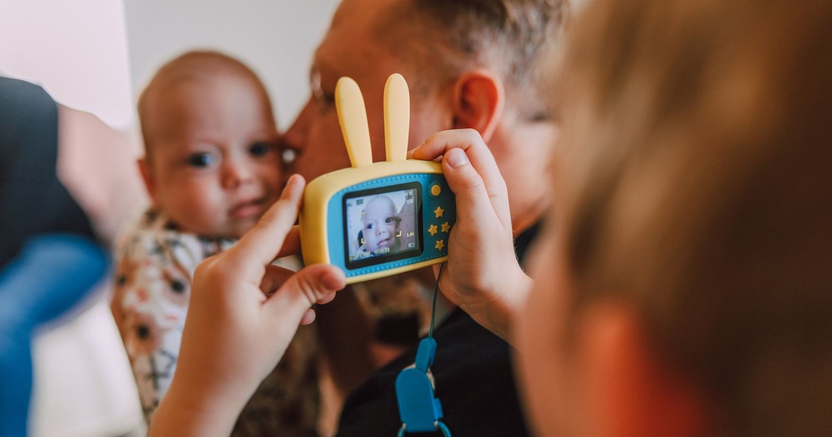 Father and child enjoying a playful moment with a toy camera indoors.