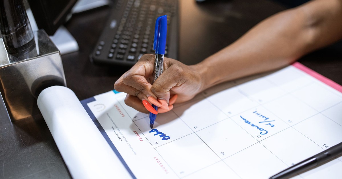 Detailed shot of a person's hand writing notes on a calendar using a blue marker.