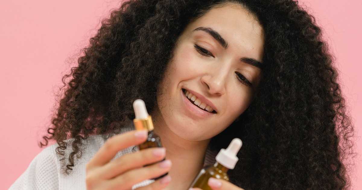 A young woman analyzes skincare bottles, set against a pink backdrop.