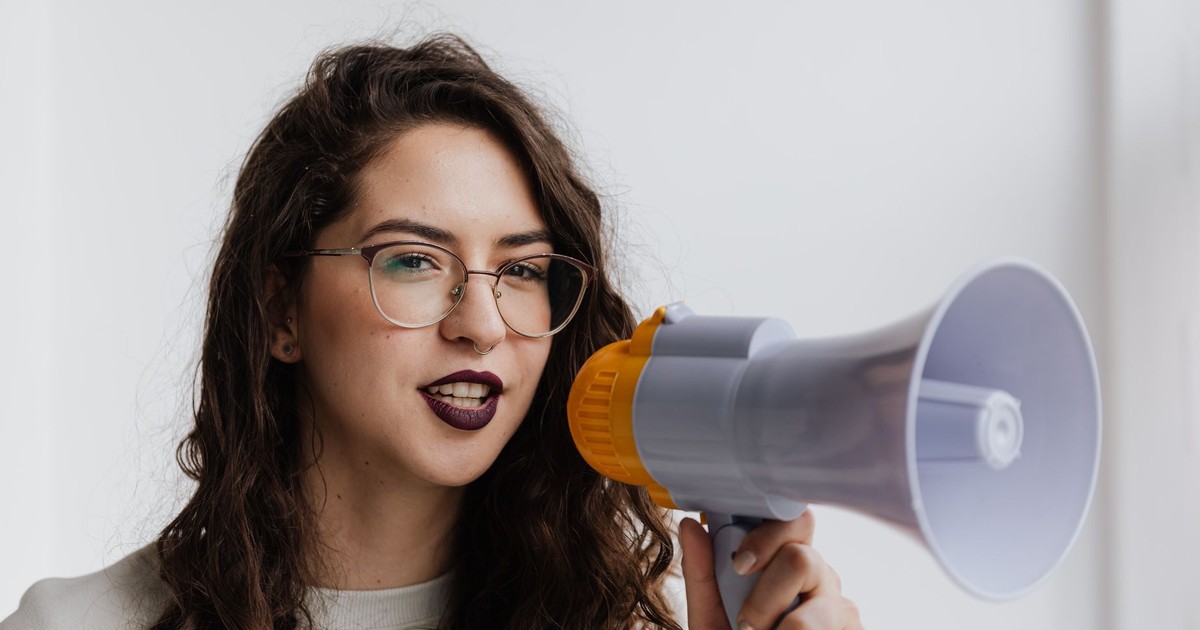 Confident woman with eyeglasses speaking into a megaphone in a bright room.