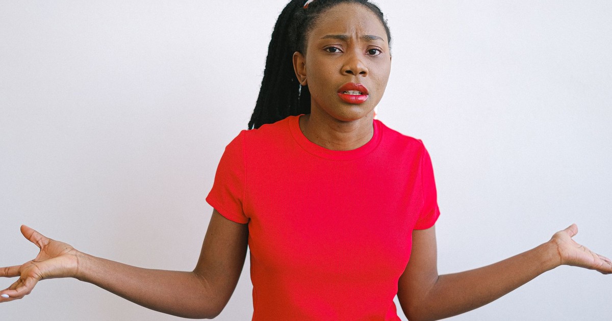 Young black woman in a red shirt with a confused expression. Perfect for emotive stock photo needs.