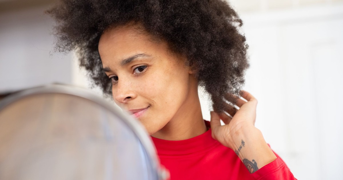 Confident woman with afro hairstyle glancing in the mirror, adjusting her hair indoors.