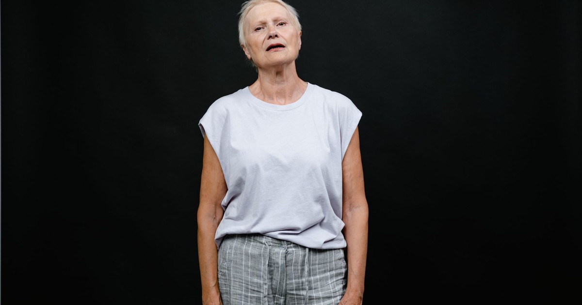 Elderly woman in a studio with a contemplative expression on a black background.