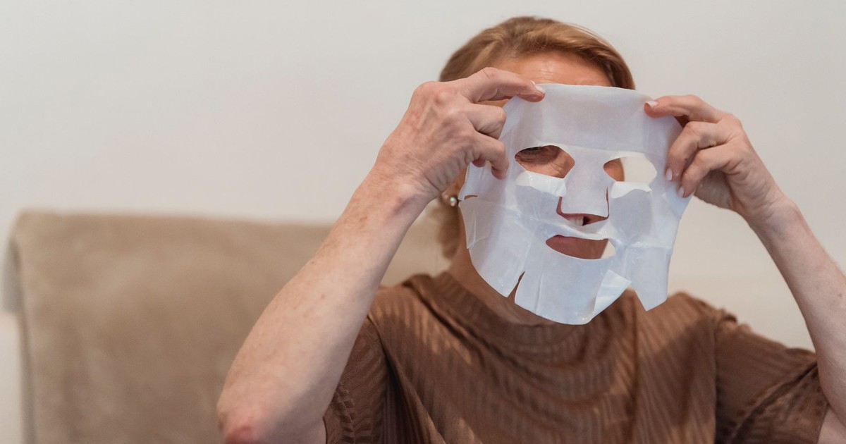 Senior woman applying a sheet face mask for skincare and relaxation indoors.