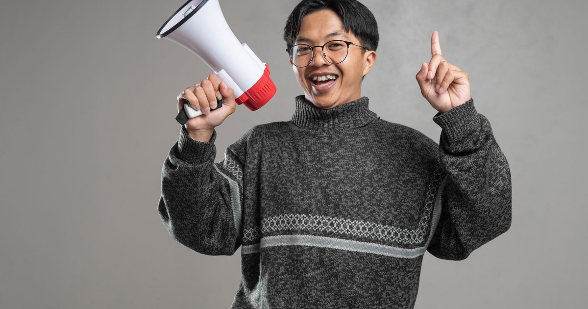 Cheerful man in sweater holding a megaphone and gesturing upward with enthusiasm.