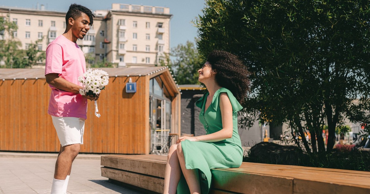 Man surprises woman with flowers in a romantic outdoor setting.