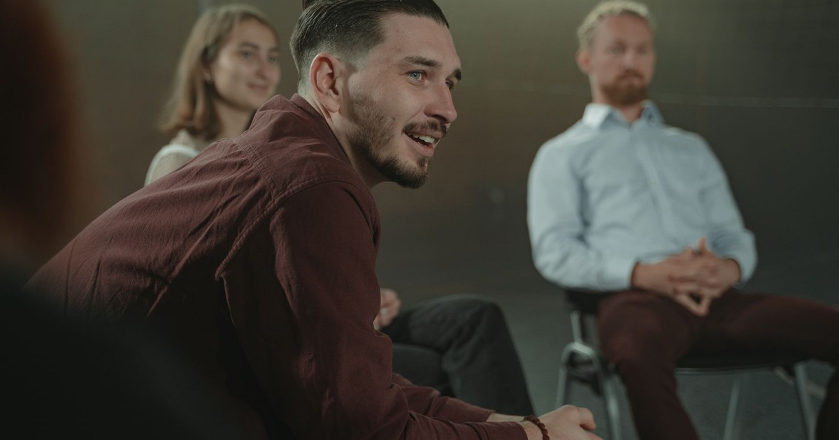 Adults sitting in a circle engaged in a group discussion indoors.
