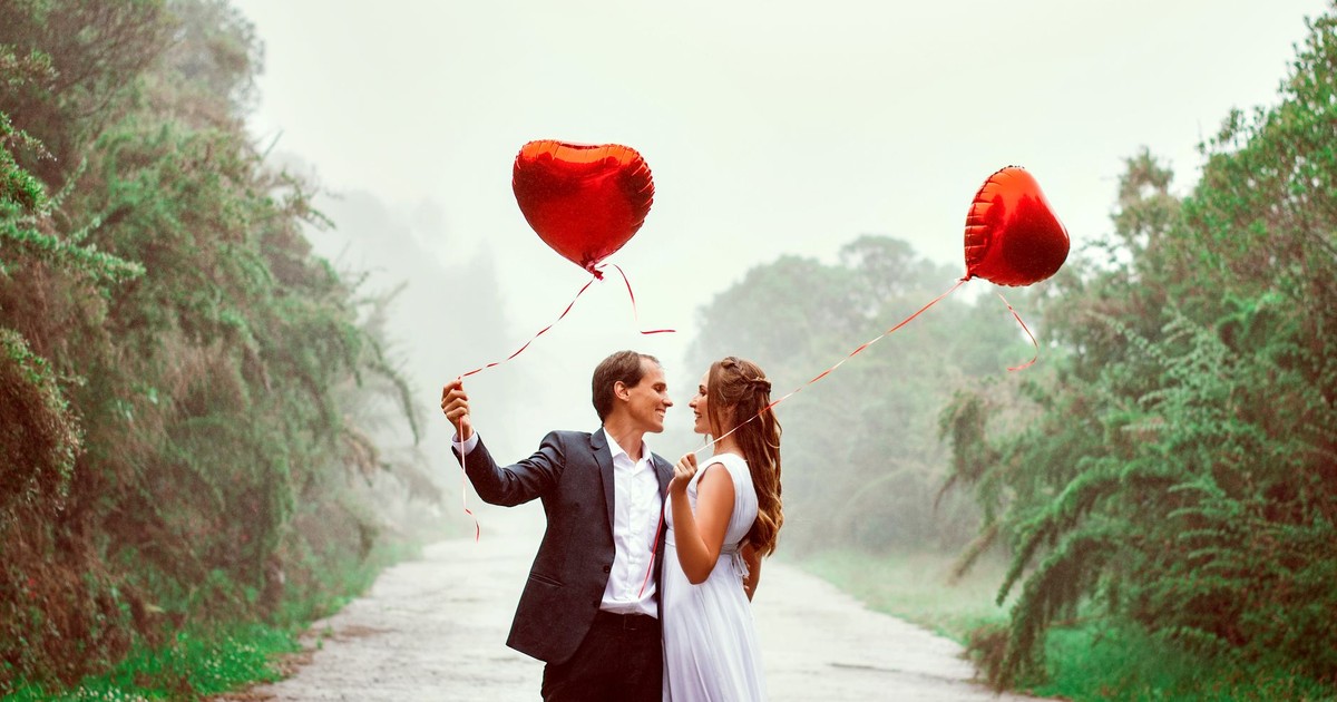 A loving couple embraces with heart-shaped balloons in a foggy park setting.