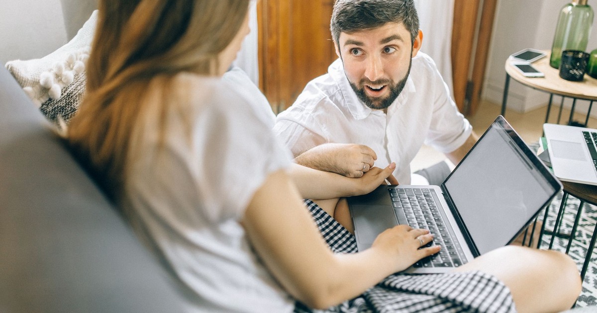 Couple working together from home on laptops, engaged in conversation.