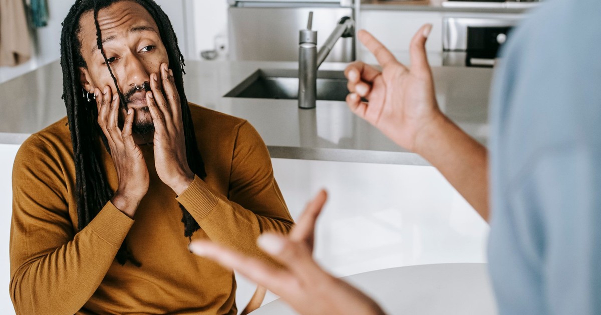 Young African American male sitting at table with hands on face and having conflict with female on kitchen