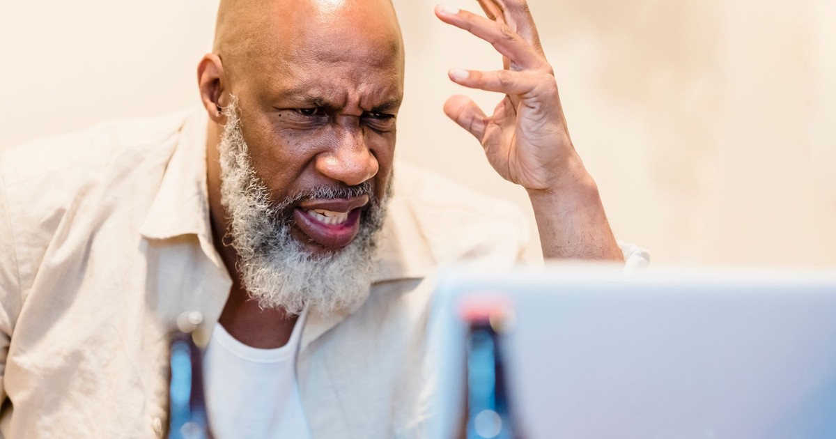 An adult man expressing frustration during a video call with a laptop indoors.