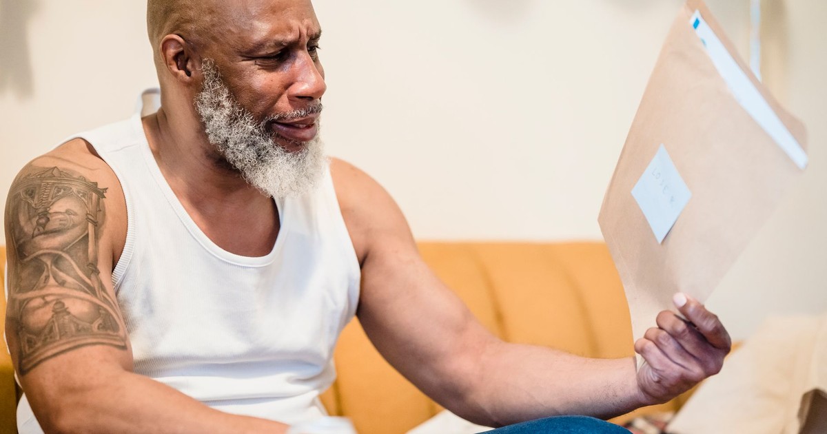 Senior man looking stressed while reading financial documents at home.