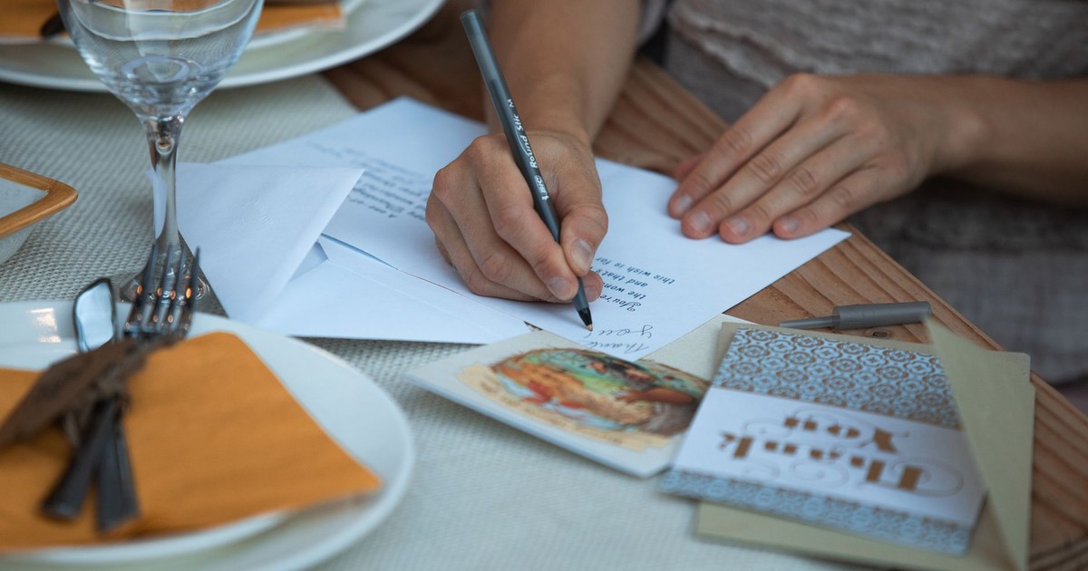 Woman writing thank you notes at a Thanksgiving dinner table setting.