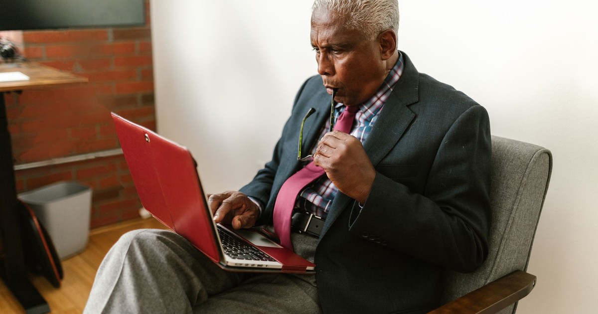 Senior man in business suit intensely focused on laptop in modern office setting.