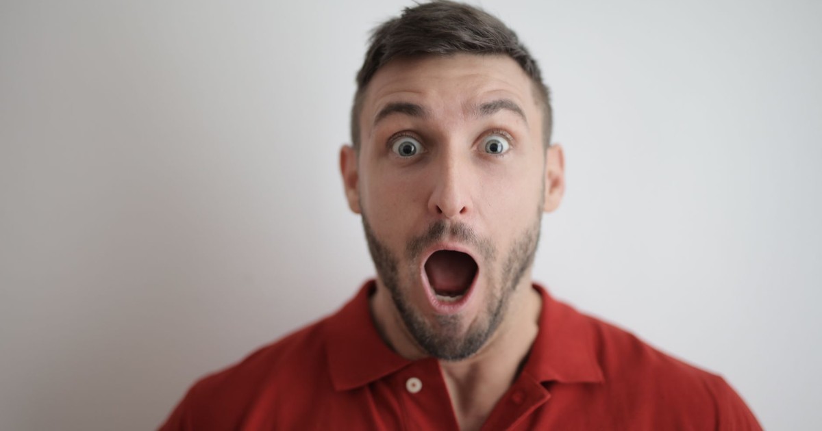 Portrait of a shocked man in a red polo shirt with a white background, expressing surprise.
