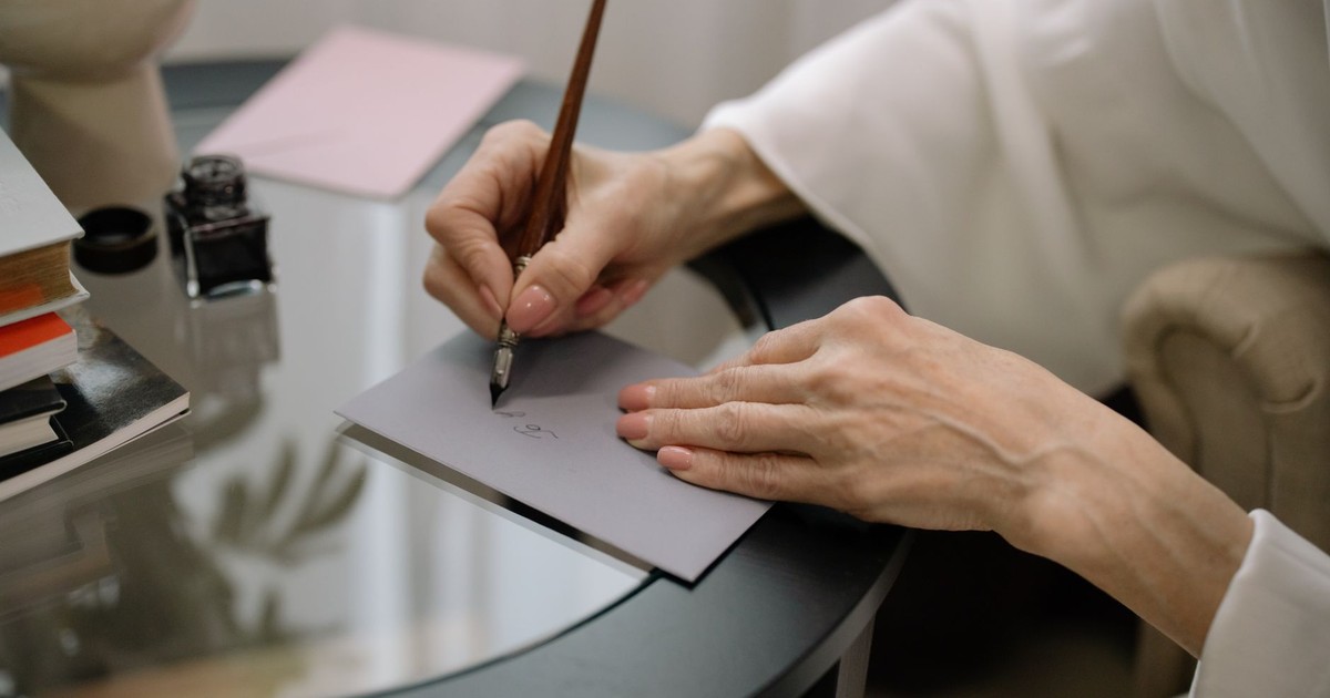 Close-up of hands elegantly writing on a gray envelope using a fountain pen.