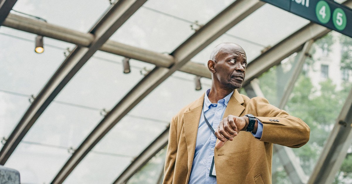 Serious African American businessman in formal clothes standing in subway station and checking time on wristwatch while looking away thoughtfully