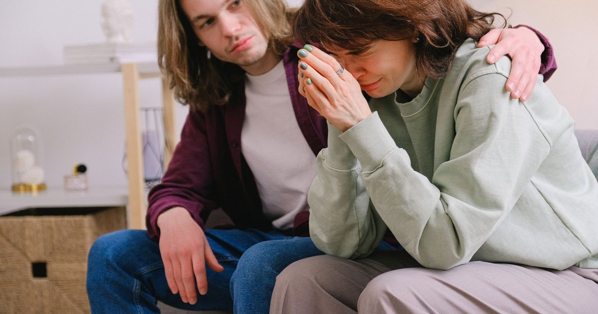 Crop male soothing disappointed crying female in sweatshirt and gray trousers on blurred background