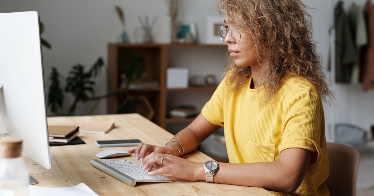 A woman working remotely from home, typing on a keyboard at her work desk.