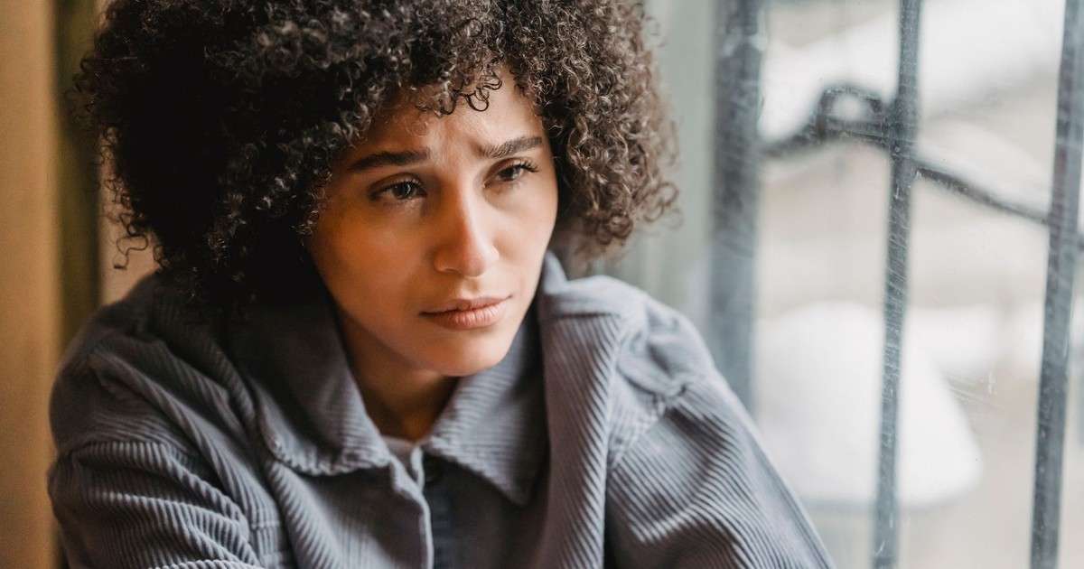 High angle of crop African American female in despair with frown face suffering from trouble sitting near window