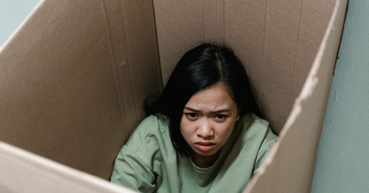 A woman inside a cardboard box symbolizes feelings of anxiety and claustrophobia.