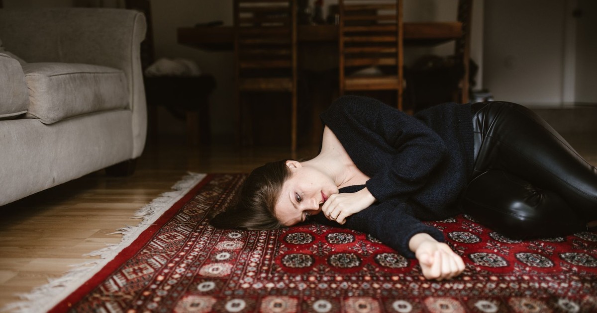 A contemplative woman resting on an intricate oriental rug in a cozy living space.