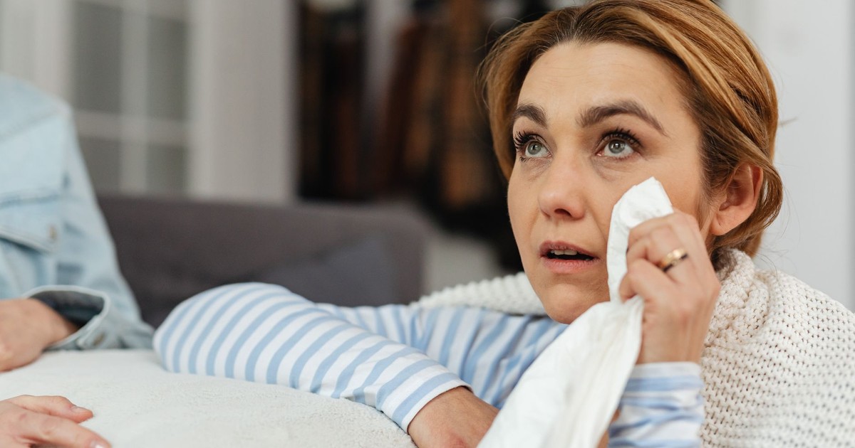 A woman wipes her tears with a tissue, expressing emotions while indoors.