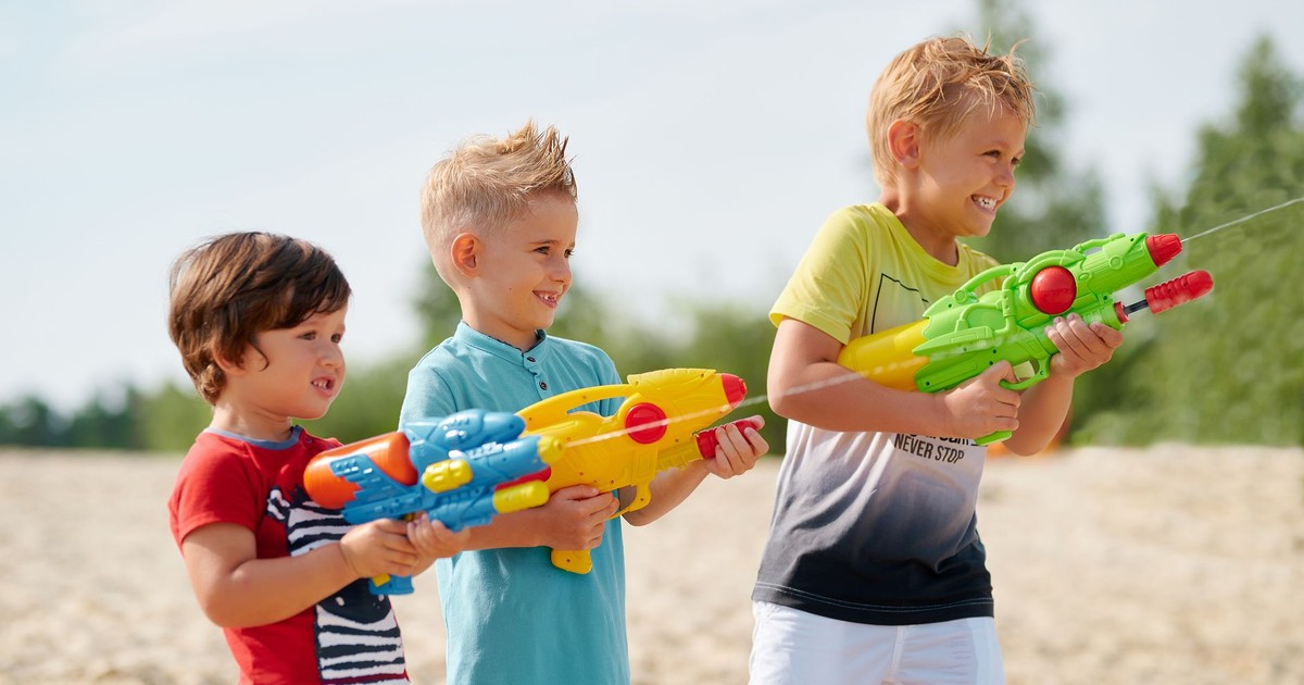 Three young boys enjoy playing with colorful water guns on a sunny beach day.