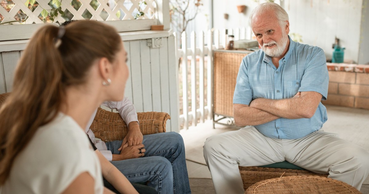 Senior man and two adults having a friendly conversation on a spacious veranda.
