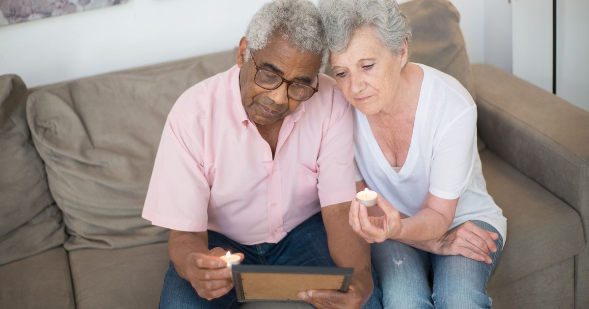 An elderly couple sits on a sofa with a picture frame, reflecting with candles.