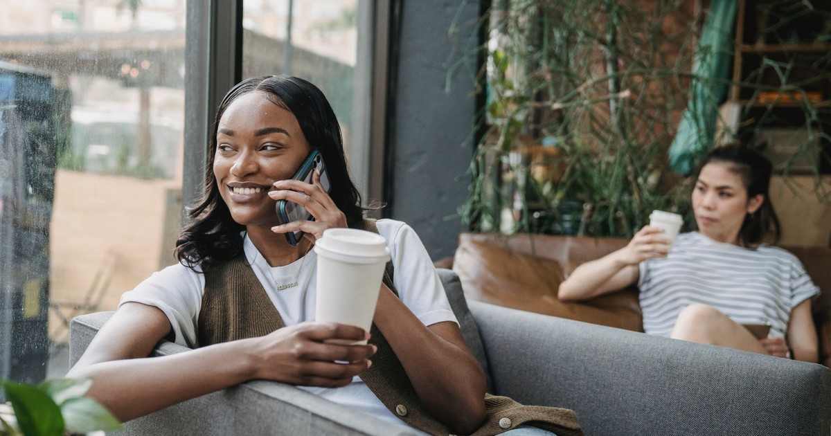 Two women enjoying coffee and a phone call in a cozy, urban café setting.