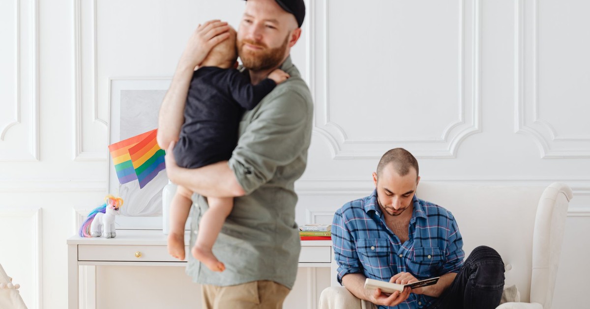 Two men and a child in a modern living room, showcasing family diversity and love.