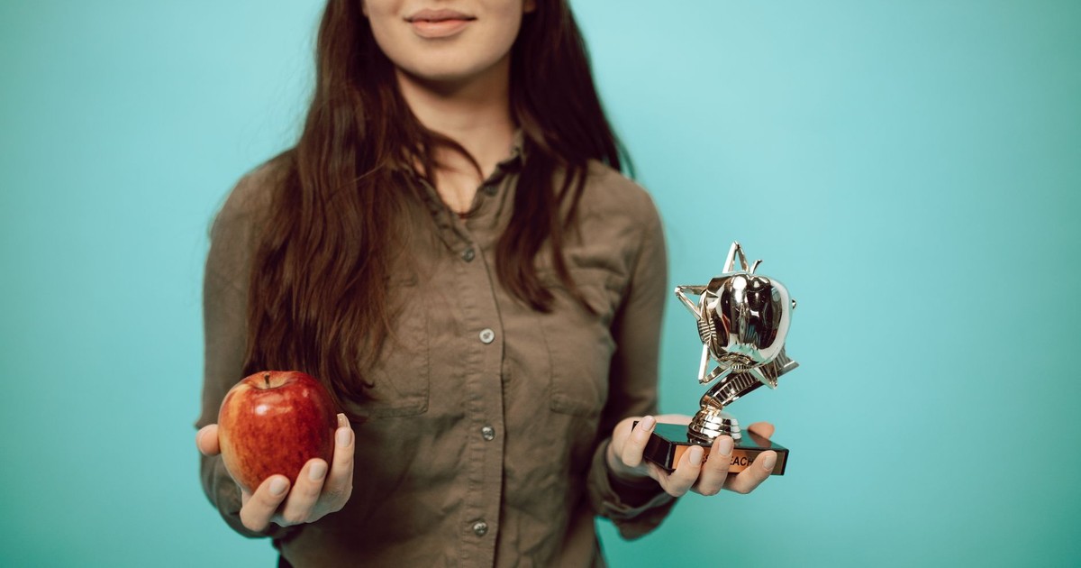 Woman holding an award trophy and apple against a turquoise background, symbolizing achievement and balance.