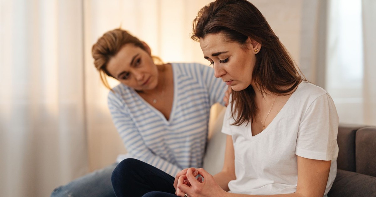 Two women sitting on a couch, sharing emotional support and connection in a warm living room setting.