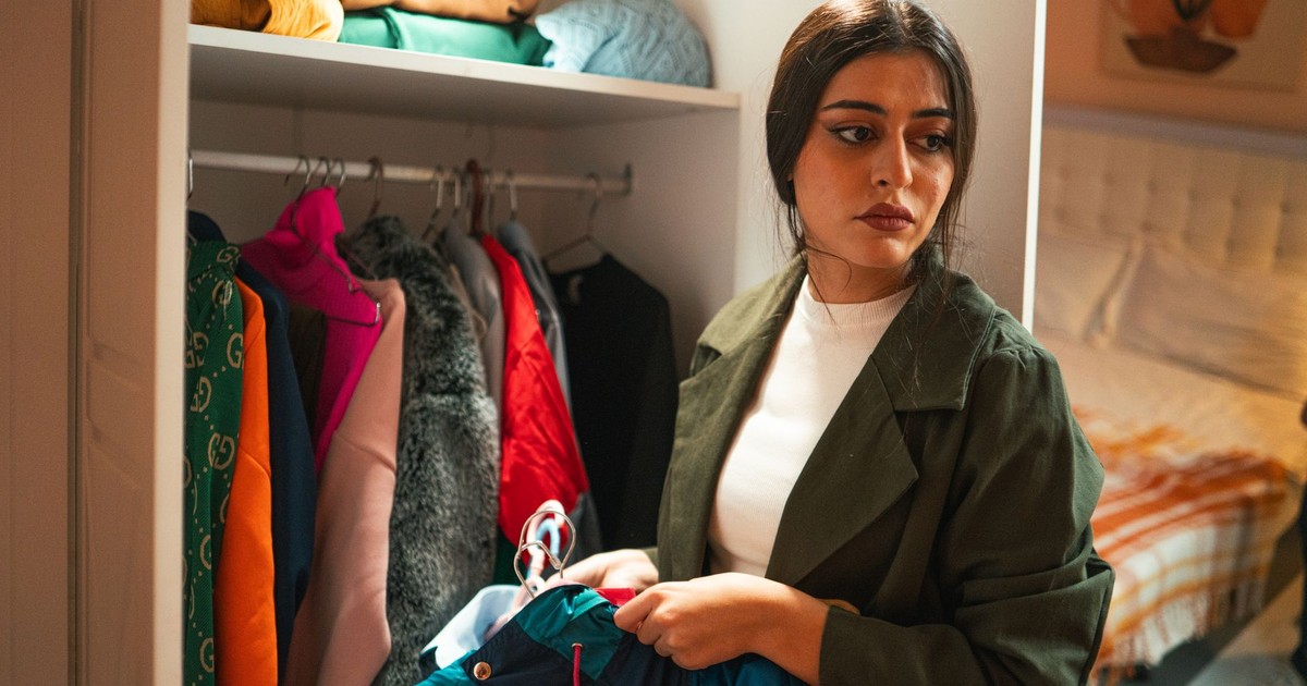 Woman organizing clothes in a closet with thoughtful expression in a modern bedroom.
